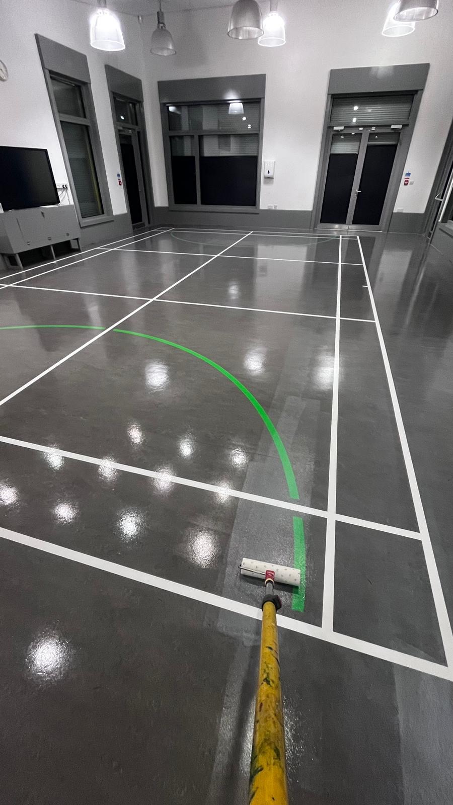 Applying a green court line by roller onto a newly sealed resilient sports hall floor
